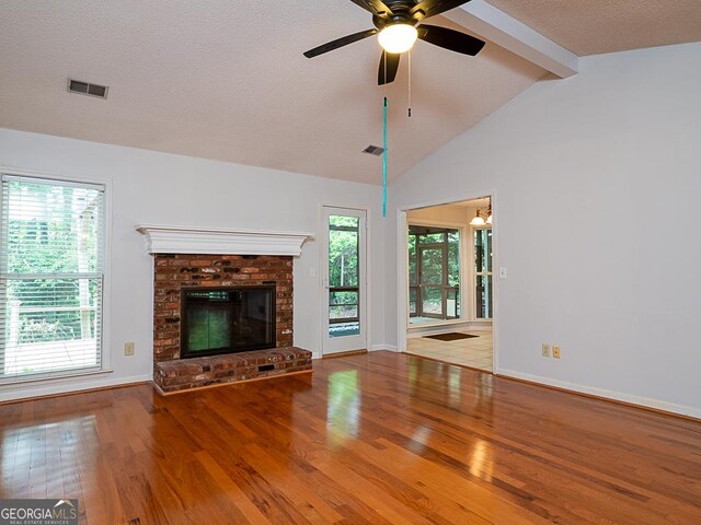 unfurnished living room with wood finished floors, a ceiling fan, a fireplace, plenty of natural light, and a textured ceiling