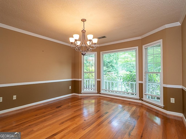 empty room featuring a chandelier, wood finished floors, a textured ceiling, baseboards, and ornamental molding