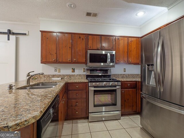 kitchen with stainless steel appliances, a sink, ornamental molding, a textured ceiling, and brown cabinets