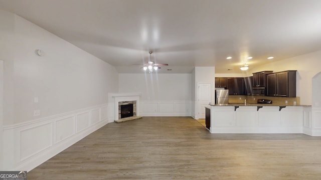 900 Ellesmere Pt, Mcdonough, GA 30253 - unfurnished living room with a decorative wall, ceiling fan, a stone fireplace, a wainscoted wall, and light wood-type flooring