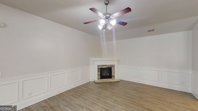 900 Ellesmere Pt, Mcdonough, GA 30253 - unfurnished living room with a stone fireplace, ceiling fan, light wood-type flooring, wainscoting, and a decorative wall