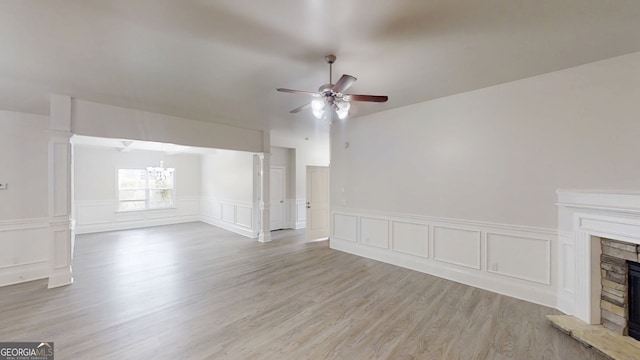 900 Ellesmere Pt, Mcdonough, GA 30253 - unfurnished living room with a fireplace with raised hearth, a chandelier, ceiling fan, light wood-style floors, and a wainscoted wall