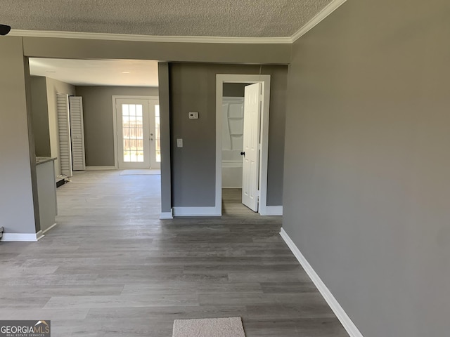 corridor featuring a textured ceiling, ornamental molding, baseboards, wood finished floors, and french doors