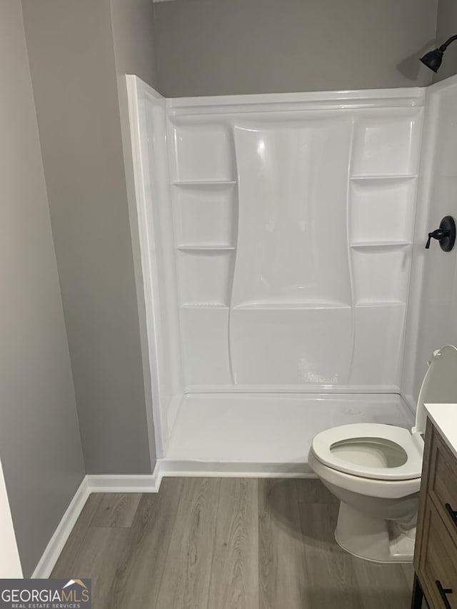 full bath featuring a shower, vanity, wood finished floors, toilet, and baseboards