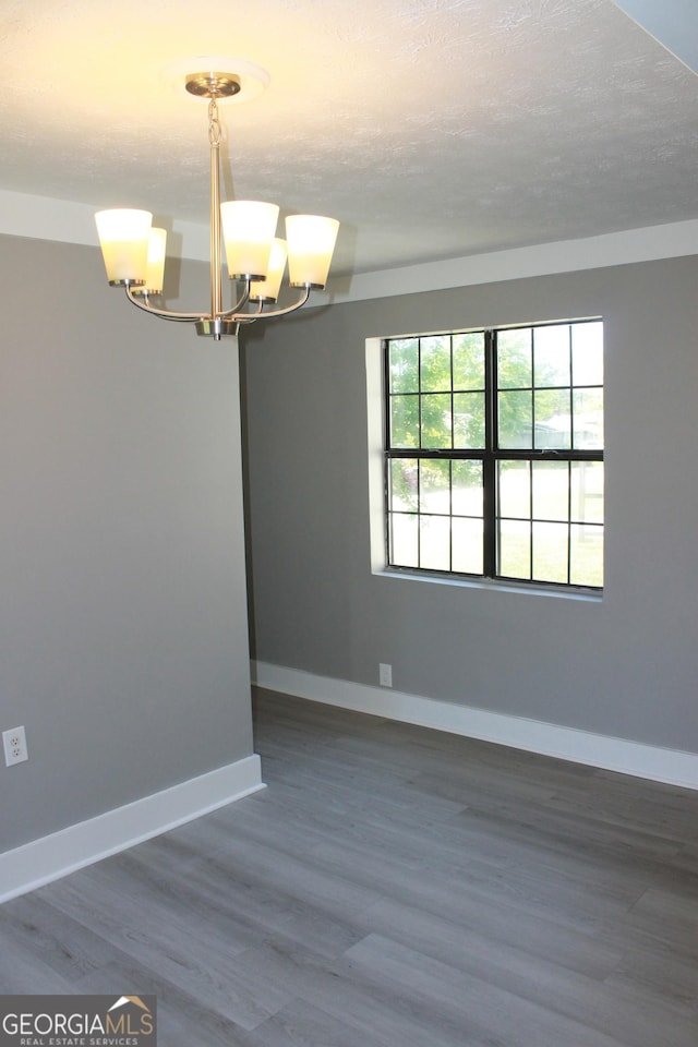 empty room with a chandelier, baseboards, and wood finished floors