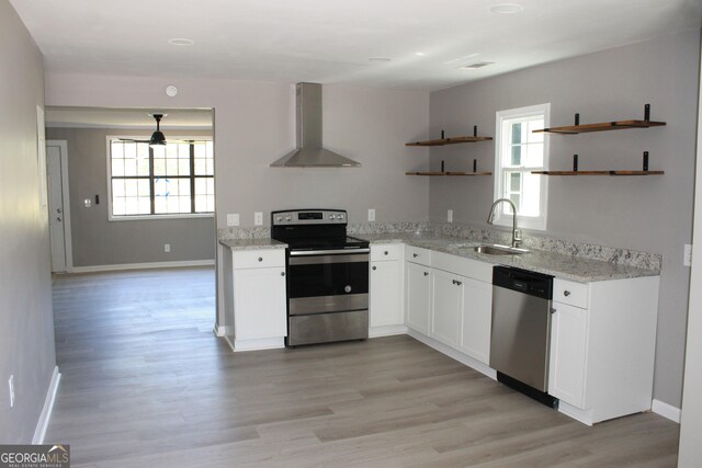 kitchen with stainless steel appliances, wall chimney exhaust hood, a sink, open shelves, and plenty of natural light