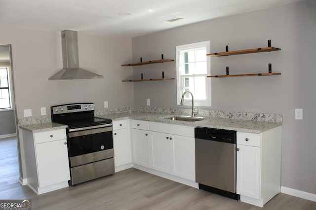 kitchen with open shelves, wall chimney range hood, stainless steel appliances, a sink, and light wood-type flooring