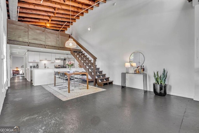 living room featuring a towering ceiling, stairway, concrete floors, and baseboards