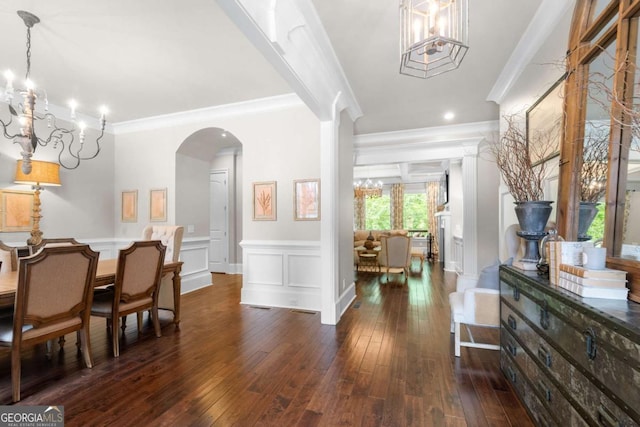 foyer entrance with a chandelier, dark wood finished floors, ornamental molding, arched walkways, and wainscoting