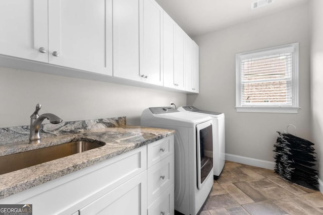 laundry area featuring independent washer and dryer, cabinet space, baseboards, and light stone finish flooring