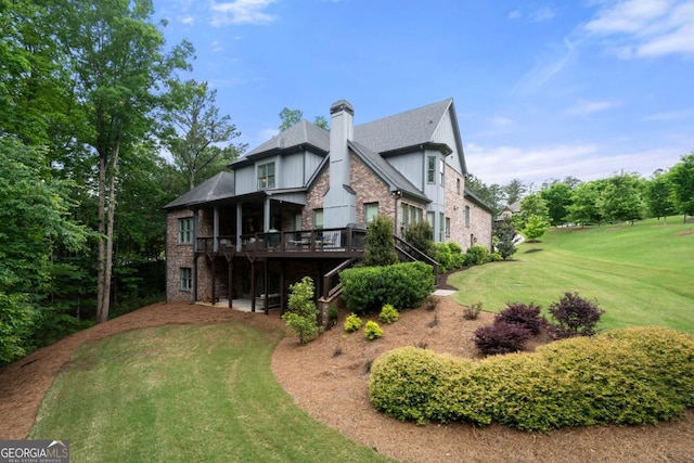 rear view of house with a chimney, a deck, a yard, brick siding, and a shingled roof