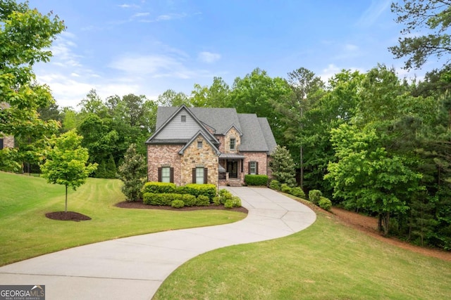 view of front of house featuring stone siding, driveway, a front yard, and view of scattered trees