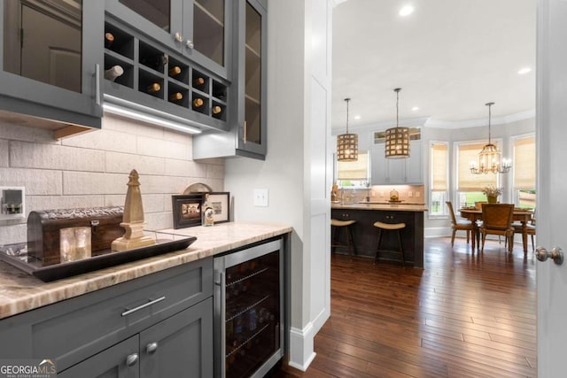 bar area featuring beverage cooler, crown molding, decorative backsplash, dark wood-style floors, and pendant lighting