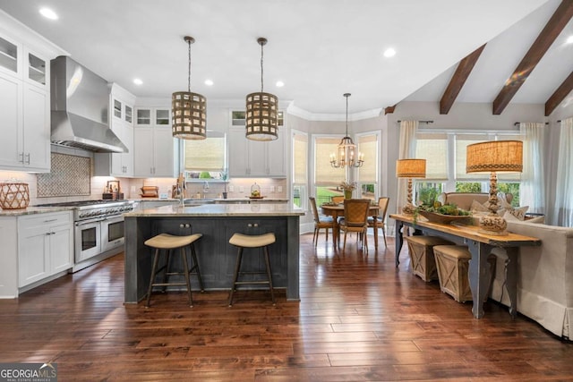 kitchen with double oven range, wall chimney range hood, a chandelier, a center island with sink, and dark wood finished floors
