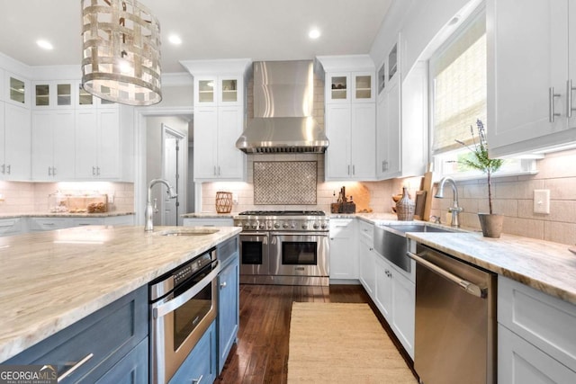 kitchen with wall chimney exhaust hood, stainless steel appliances, a sink, white cabinetry, and tasteful backsplash
