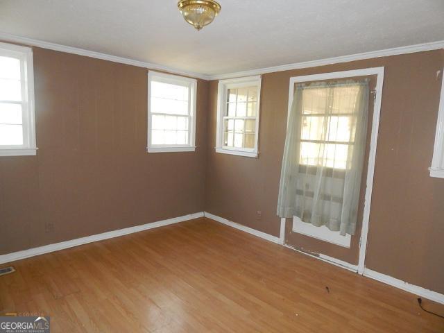 unfurnished room with wood finished floors, baseboards, and crown molding