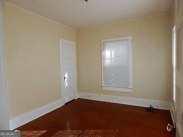 empty room with dark wood-style floors, baseboards, and ornamental molding