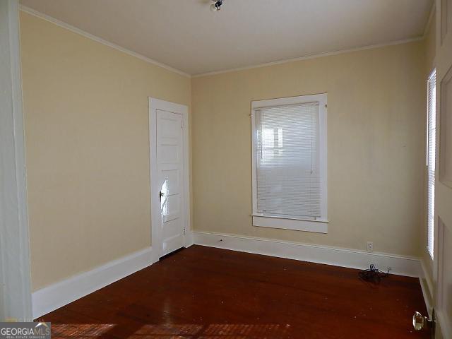 unfurnished room featuring dark wood-style flooring, baseboards, and ornamental molding