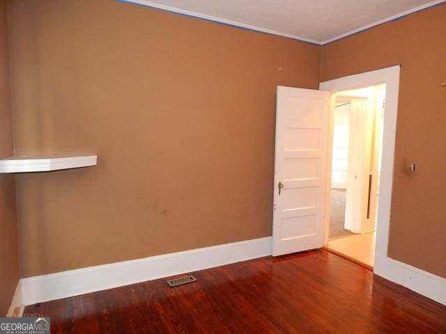 empty room with wood finished floors, baseboards, and ornamental molding