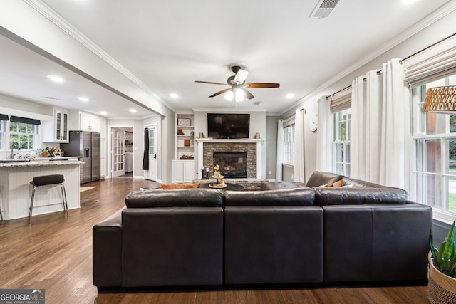living area featuring ornamental molding, a ceiling fan, a stone fireplace, dark wood-style flooring, and recessed lighting