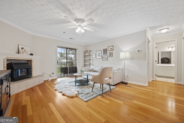 970 Sidney Marcus Blvd Unit 2403, Atlanta, GA 30324 - living room featuring light wood-type flooring, ceiling fan, a tiled fireplace, ornamental molding, and a textured ceiling