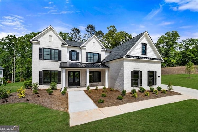 view of front of property with a standing seam roof, a front lawn, roof with shingles, brick siding, and a porch
