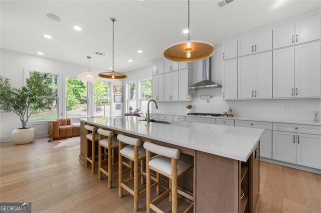 kitchen with wall chimney range hood, a sink, recessed lighting, light wood-type flooring, and light countertops