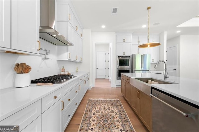 kitchen featuring appliances with stainless steel finishes, wall chimney exhaust hood, a sink, light countertops, and white cabinets