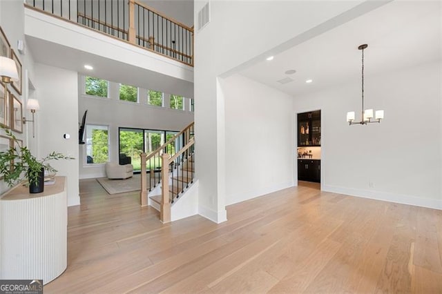 foyer featuring a chandelier, light wood finished floors, a high ceiling, stairway, and baseboards