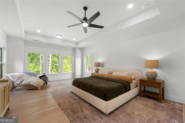 bedroom with a raised ceiling, baseboards, wood finished floors, recessed lighting, and a ceiling fan