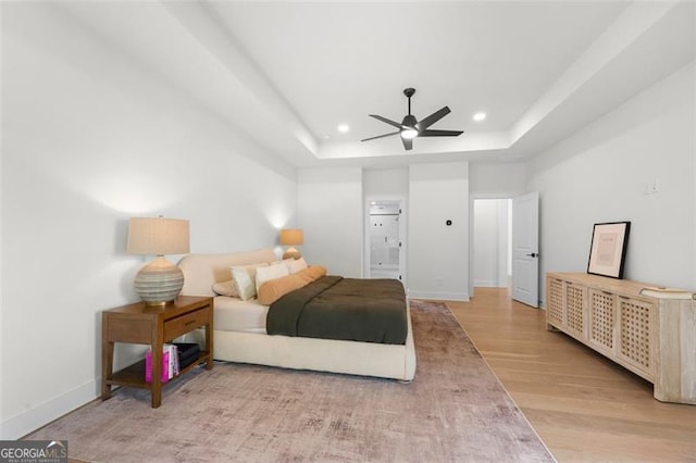 bedroom featuring recessed lighting, light wood-type flooring, a raised ceiling, baseboards, and ensuite bath