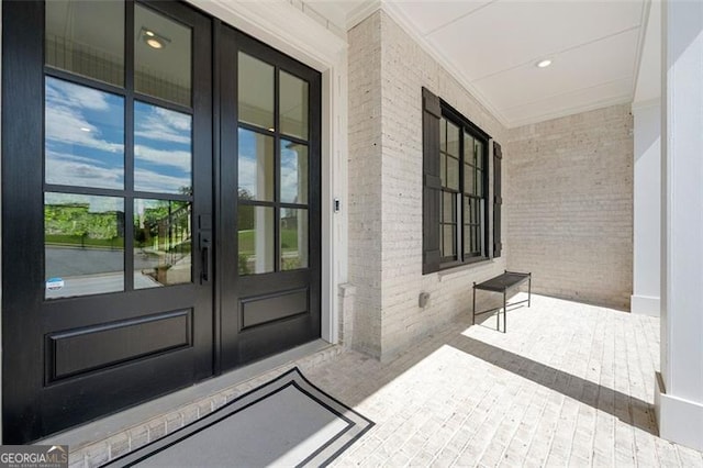 doorway to property featuring brick siding, covered porch, and french doors