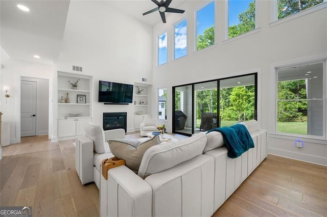 living room featuring a glass covered fireplace, baseboards, ceiling fan, a high ceiling, and light wood-style floors
