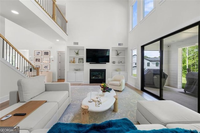17145 River Overlook Dr, Roswell, GA 30075 - living room with a towering ceiling, wood finished floors, a glass covered fireplace, stairway, and built in features