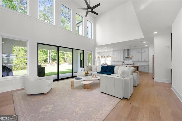 living area featuring a high ceiling, a ceiling fan, light wood-style flooring, baseboards, and healthy amount of natural light