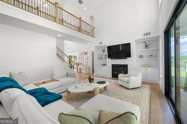 living area featuring wood finished floors, a towering ceiling, stairs, a glass covered fireplace, and built in features
