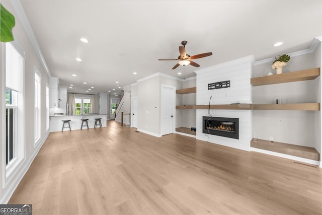 unfurnished living room featuring crown molding, a fireplace, recessed lighting, a ceiling fan, and light wood-style flooring