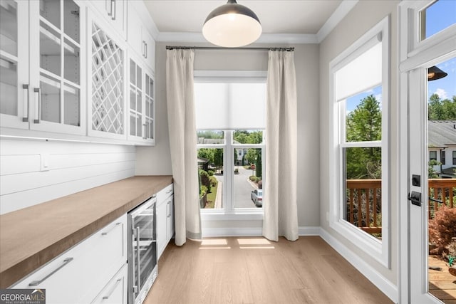 doorway to outside featuring beverage cooler, light wood-type flooring, a bar, ornamental molding, and baseboards