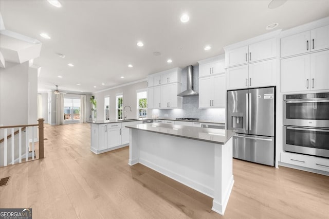 kitchen with stainless steel appliances, wall chimney range hood, a peninsula, light wood-type flooring, and a sink