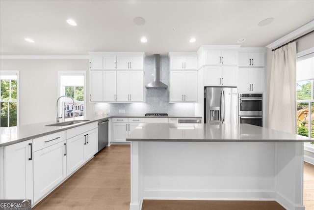 kitchen with stainless steel appliances, wall chimney range hood, a sink, backsplash, and healthy amount of natural light