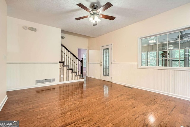510 Aiken Dr, Dallas, GA 30157 - unfurnished living room featuring wood finished floors, ceiling fan, a textured ceiling, a wainscoted wall, and stairway