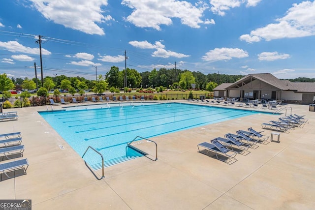 community pool with fence, a patio, and view of wooded area