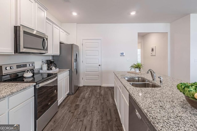 kitchen featuring appliances with stainless steel finishes, a sink, dark wood finished floors, white cabinets, and light stone countertops