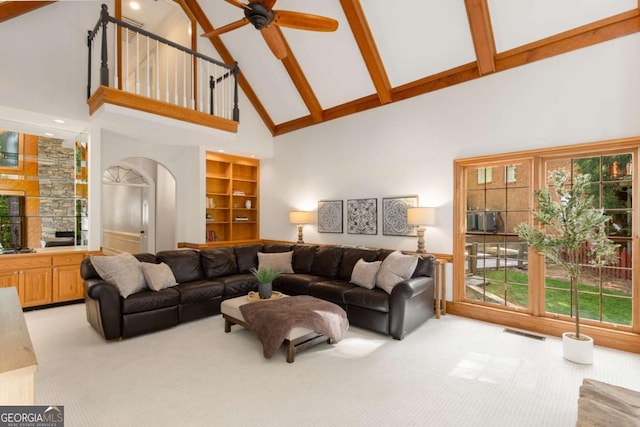 living room with high vaulted ceiling, light carpet, arched walkways, beam ceiling, and a ceiling fan