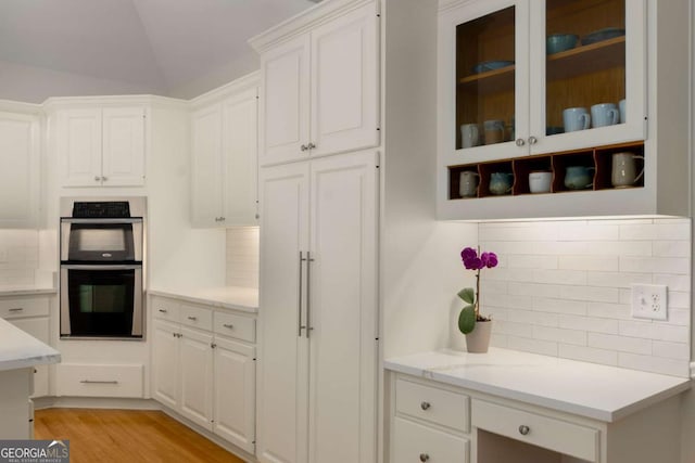 kitchen featuring double oven, white cabinets, tasteful backsplash, light wood-style floors, and lofted ceiling