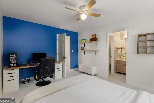 bedroom featuring light colored carpet, a desk, baseboards, ceiling fan, and ensuite bath