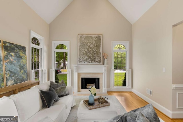living room featuring wood finished floors, a fireplace, baseboards, and high vaulted ceiling