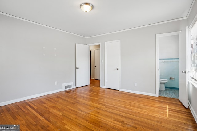 unfurnished bedroom with light wood-style flooring, crown molding, ensuite bathroom, and baseboards