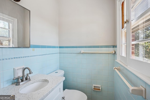half bath with tile walls, toilet, a wainscoted wall, and vanity