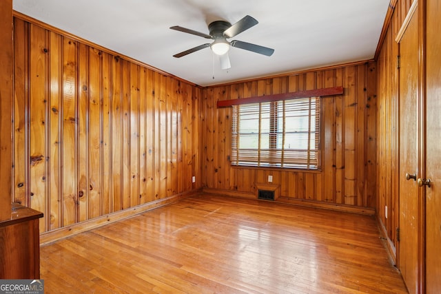 unfurnished room featuring light wood-style flooring, ceiling fan, and wooden walls